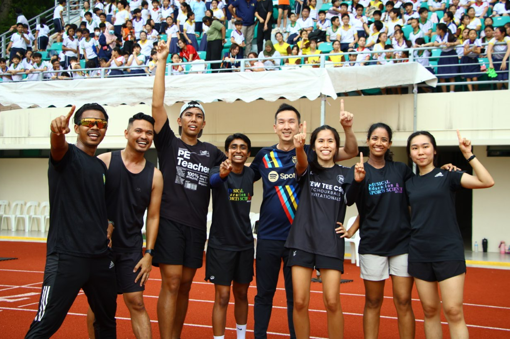 A group of staff members cheer enthusiastically, showing their strong team spirit, unity and support for the school community.